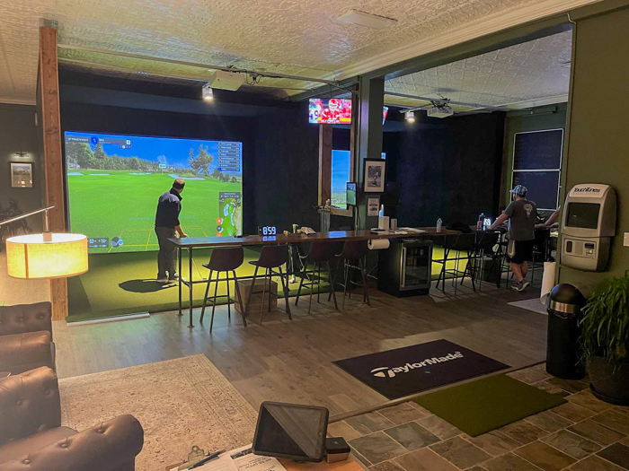 A photograph of golfers playing indoor simulator golf at Miller Mulligans in Pittsburgh, Pa